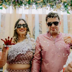 A fun-filled moment from a Haldi ceremony, with the couple wearing sunglasses and being showered with flower petals. We capture the playful side of wedding rituals.