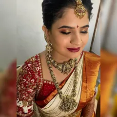 A close up of a traditional South Indian bridal makeup look. The focus is on the golden shimmery eyeshadow, perfectly winged eyeliner, and a deep red lip, set against flawless skin. This look is designed to last through all the wedding day ceremonies.