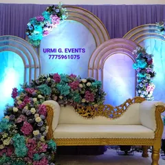 I love creating these lush, floral-heavy designs for a truly romantic anniversary celebration. This stage features a cascade of purple, blue, and pink flowers flowing over an elegant white and gold sofa, set against backlit arched panels.