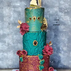 For this grand wedding celebration, I designed a three-tiered cake with rich jewel tones. Each tier features a different non-fondant texture, from a quilted pattern to geometric embossing and a gold-stenciled base, all brought together with deep red sugar flowers.