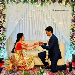 A picture-perfect proposal moment during an engagement ceremony, set against a backdrop of a floral arch and white drapes.