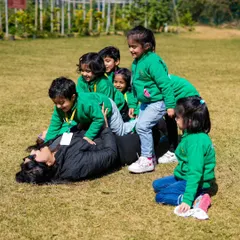A joyful moment as a group of students playfully pile on top of their teacher on the grass.