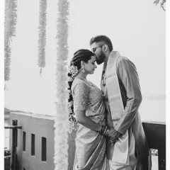 A timeless black and white portrait. The groom's gentle kiss on the bride's forehead speaks volumes, capturing a moment of tenderness and protection against a soft, beautiful backdrop.