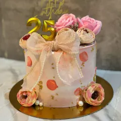 A lovely bow cake for a 25th birthday. This pink cake is decorated with a large, handcrafted bow, pearl details, and delicate sugar flowers.