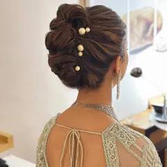 A closer look at a "perfectly undone" textured updo. The interwoven sections create volume and dimension, while the scattered pearl pins add a touch of modern elegance, making it a popular choice for reception looks.