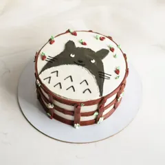 A cute hand-painted cake featuring Totoro from Studio Ghibli. The design is framed with a piped border and tiny strawberries, making it a whimsical treat for an anime fan.