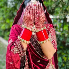 The classic bridal pose, highlighting the rich, dark stain of the full-hand mehndi design. The intricate patterns on her palms are a testament to traditional henna artistry.