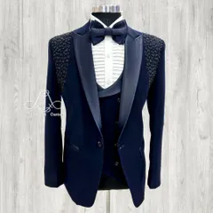A navy blue three-piece tuxedo with a modern twist. The shoulders feature a textured, beaded pattern, adding a unique detail to the classic satin shawl collar and pleated formal shirt.