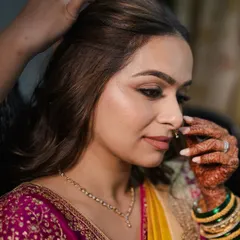 A quiet moment during hair styling. The makeup is already done, showcasing a flawless base and a soft, defined eye, ready for the final hairstyle.