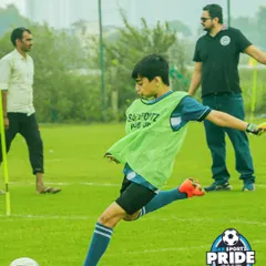 A player in a green training bib practices his shooting form, striking the ball with precision during a warm-up session at the Pride Cup.
