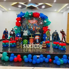 This is an action-packed Avengers theme party I designed for a 10th birthday. The stage features a custom backdrop with all the major superheroes, character cutouts of Batman, Superman, and Iron Man, and balloon columns in the classic red, blue, and green superhero colors.