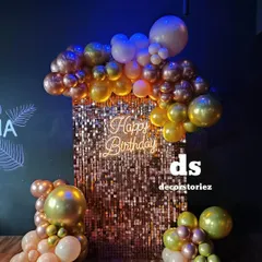 This close-up shows a glamorous photo corner we designed, featuring a shimmering rose gold sequin wall. The setup is framed by a cascade of metallic balloons and a 'Happy Birthday' neon sign, creating a perfect spot for party pictures.