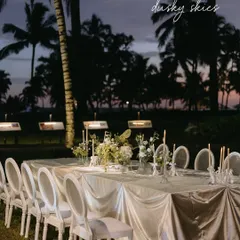 An elegant dinner party set against the backdrop of a Goan sunset. The long table is draped in shimmering fabric, with classic white chairs and soft candlelight creating a timeless and romantic scene.
