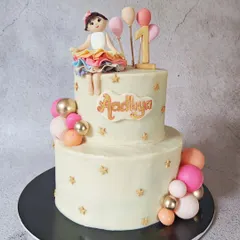 This two-tier cake was designed for a sweet first birthday. It features a simple, elegant design with a cascade of pink, peach, and gold chocolate spheres and a handcrafted fondant doll on top.