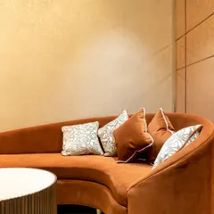 Comfort is key to a luxurious shopping experience. This custom-designed curved sofa in a rich terracotta velvet provides a soft, inviting seating area, set against a wall with subtle, textured wallpaper.