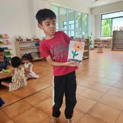 A young boy proudly shows off his finished flower collage. The smile of accomplishment is the true goal of our art activities.