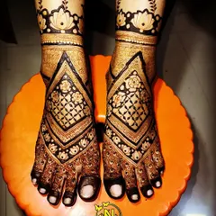 A geometric style bridal feet design with bold, diamond shaped patterns. The dark henna stain creates a striking contrast, making the design stand out.