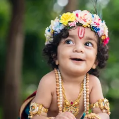 An adorable upward-looking shot of a baby boy dressed as Krishna, with a beautiful, innocent smile.