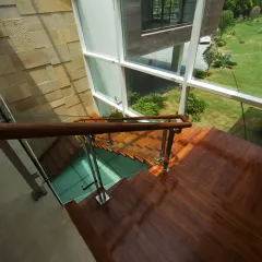 This staircase in the Sachdeva Farmhouse is enclosed within expansive glass panels, bathing the space in natural light and framing views of the garden. The warm wooden treads contrast with the textured Indian stone walls.