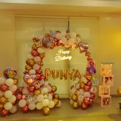 A beautiful balloon arch in rose gold, gold, and white for "PUNYA". This setup includes a neon sign, character accents, and transparent boxes that can be filled with balloons or other items.