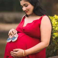 A sweet and symbolic outdoor maternity photo. The mother-to-be holds a tiny pair of baby shoes against her bump, signifying the new life to come.