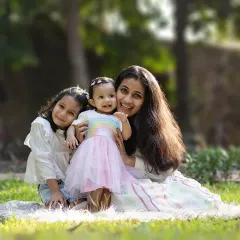 A mother holding her two daughters close. The warm sunlight and green surroundings make this outdoor family portrait feel so full of life and happiness.