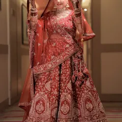 A classic bridal portrait. The bride, in her traditional red lehenga, lifts her veil, her confident smile capturing the essence of modern royalty.