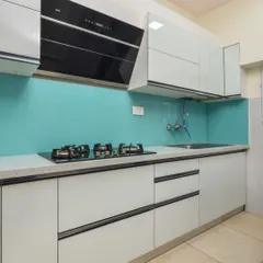 A sleek, modern kitchen with handleless white cabinets and a stunning turquoise glass backsplash. The design includes a built-in hob and chimney for a seamless and minimalist look.