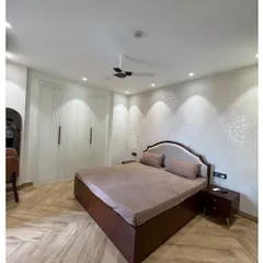 A serene bedroom with herringbone wooden flooring and full-height white wardrobes that provide ample storage. The subtle stencil work on the wall adds a touch of traditional elegance.