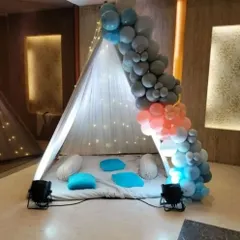 A simple and modern teepee tent decorated with a balloon garland in shades of blue and grey. This setup provides a stylish and comfortable nook for any small, private celebration.