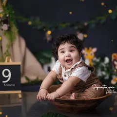 A joyful 9-month milestone shoot with a fun jungle safari theme. This little boy's excited expression is priceless as he sits in a wooden bowl, surrounded by friendly lion and giraffe props.