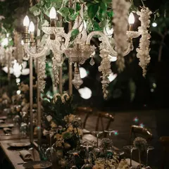 A close-up of the tablescape from a beautiful wedding dinner. The setting features elegant chandeliers dripping with white wisteria, creating a magical, intimate atmosphere for guests.