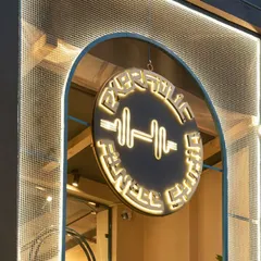 A close-up of our studio logo, illuminated at night. The dumbbell icon inside the circle represents our core focus on strength, while the design reflects our modern, premium aesthetic.