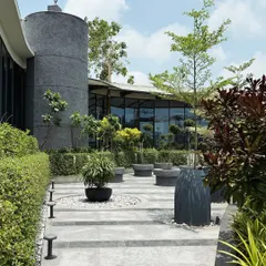 A ground-level view of the 'Stripe Play' plaza, showing the interplay of the curved building facade, striped paving, and a variety of planters. The sculpture on the cylindrical volume adds an artistic landmark.