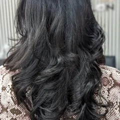 A final look at a layered haircut finished with a bouncy blowout. The curls are shaped away from the face to create volume and movement, resulting in a classic and elegant hairstyle suitable for any occasion.