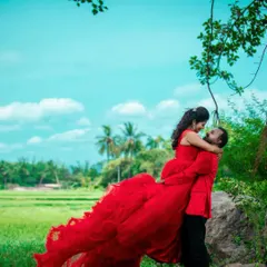 A romantic lift against a backdrop of lush green fields and a bright blue sky. This outdoor pre-wedding photo captures a moment of pure joy and connection between the couple.