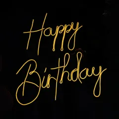 A close up of a custom 'Happy Birthday' neon sign in a warm yellow glow. These signs are a popular add on for creating a focal point at any celebration.