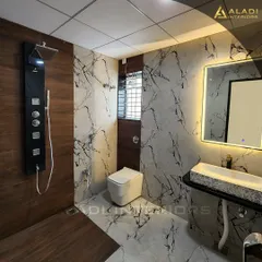 A contemporary bathroom with a mix of wood-look and marble-patterned tiles. The space is equipped with a modern black shower panel and a sleek, backlit mirror.