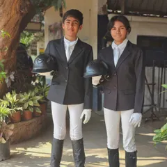 Two young riders in their formal show attire, holding their helmets. This captures the sense of pride and professionalism we foster in our equestrian team.
