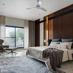 A bedroom should be a sanctuary. In this room from the Celadon residence, we combined a rich wood-paneled headboard with brass accents and soft, layered textiles. The design focuses on creating a serene retreat that feels both luxurious and deeply personal, with views oriented towards the surrounding gardens.