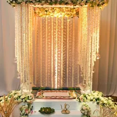 I create serene and beautiful mandaps for Navratri. This elegant setup features a canopy of white and pink flowers with hanging floral strings, creating a divine space for pooja in your home.