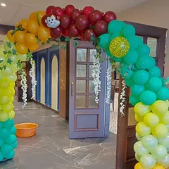 A vibrant balloon archway at the entrance of a jungle-themed party. The arch uses green, yellow, and red balloons with decorative vines to create a welcoming jungle gate for guests.