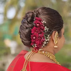A close-up of a traditional Maharashtrian bridal bun, also known as a 'khopa'. This one is a French khopa, elegantly adorned with fresh red flowers and baby's breath for a classic yet fresh look.