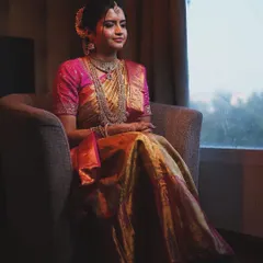 This is a candid moment of a bride on her wedding day. The makeup is soft yet defined, designed to look beautiful in any lighting. Her traditional silk saree and layered necklaces create a portrait of timeless elegance.