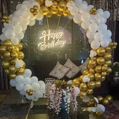 An elegant gold and white themed birthday setup in a living room. The large circular balloon arch frames the seating area perfectly, with a neon sign adding a modern touch.