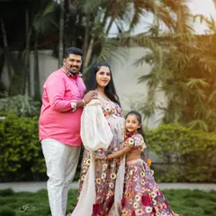 A lovely outdoor family portrait. The parents and their daughter are all wearing coordinating floral outfits, creating a cohesive and heartwarming image as they await their new family member.