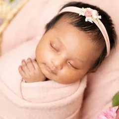 A close-up of a peacefully sleeping baby girl, wrapped in a soft pink swaddle with a delicate floral headband. My focus is on capturing their serene beauty.