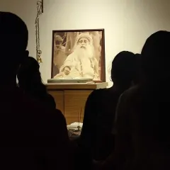 Silhouetted against the light of the Guru's presence, seekers stand in quiet reverence. The Sadhguru Sanidhi Pooja is a time for inner communion and stillness.