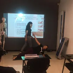 Our theory classes are interactive. A student demonstrates a core endurance test while the trainer explains the muscular engagement to the class.