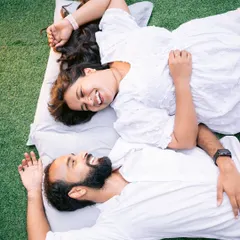 A fun and relaxed moment from a pre-wedding shoot. A couple shares a laugh while lying on the green lawn, showcasing a casual and intimate style of photography.